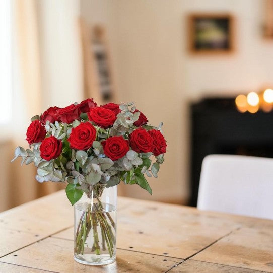 Ramo de rosas rojas en jarrón sobre mesa con velas encendidas - Floristería Peregrina